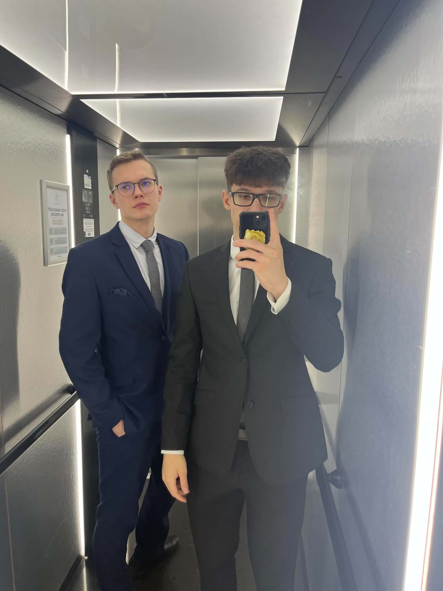 Adrián Motošický s kolegom v oblekoch pred zrkadlom